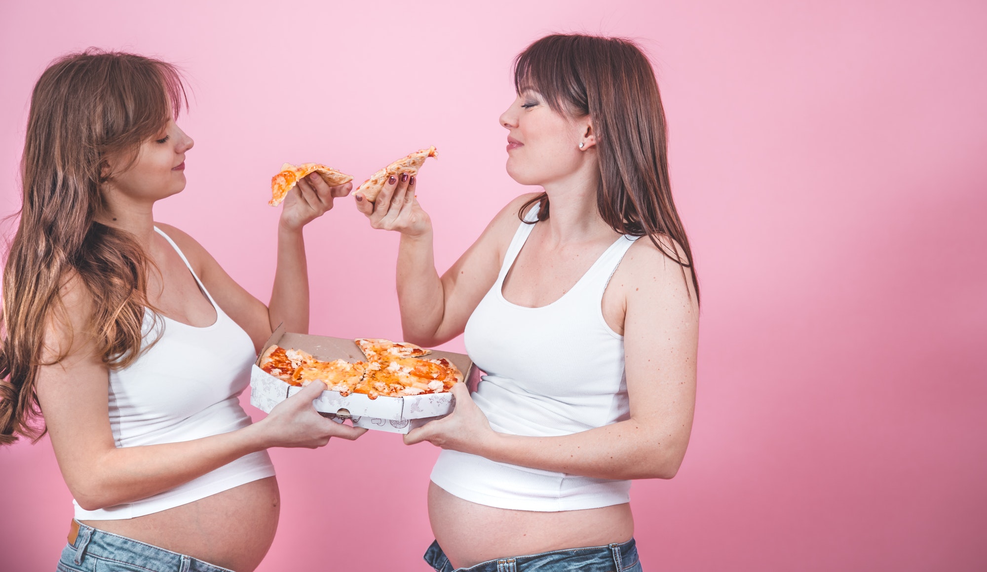 nutrition concept, pregnant women eating pizza on a pink background